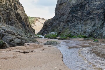 A coastal scene shows a stream flowing between rocky cliffs to the sea in Holywell Bay - Cornwall - UK
