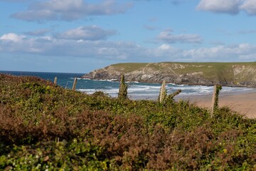 A coastal landscape is visible from a dune with a sandy beach, ocean waves and a headland in Holywell Bay - Cornwall - UK