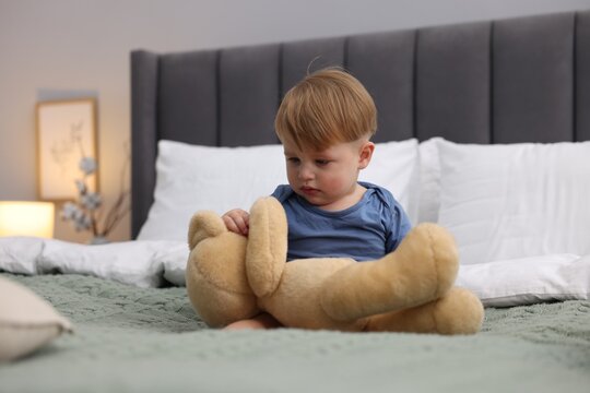 Cute little child with teddy bear in bed indoors
