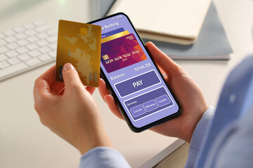 Woman with credit card using smartphone for online payment at table, closeup