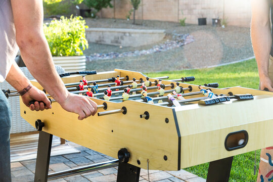 Two individuals are currently engaged in a game of foosball on a patio outside