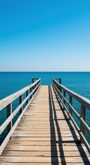 Fototapeta premium A weathered wooden dock extends over deep blue water under a clear summer sky, offering a peaceful view of the coast ,lake ,azure ,ocean