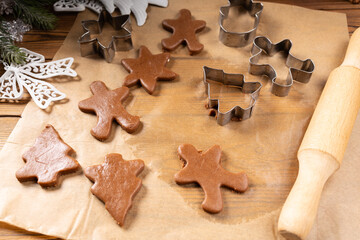 Rolled ginger dough on parchment paper, On the wooden surface there are metal gingerbread molds and a rolling pin.
