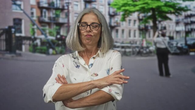 Woman points finger on street with index finger raised and arms crossed in second frame, wearing glasses and feather print blouse; disapproval.
