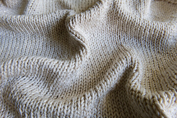 Knitted fabric texture. Cozy knit background with soft folds. Abstract background. Beige wool sweater with golden-colored metallic thread. Concept for fashion, textile, or craft projects.