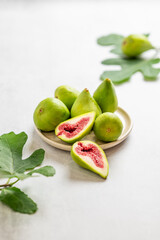 Sweet green figs on a plate, sliced, with leaves on a light background.