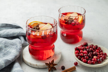 A cranberry drink in a two glasses on a light background with cinnamon, berries and napkin close up.