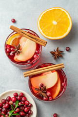 A cranberry drink in a two glasses on a light background with cinnamon, berries and citrus fruit.