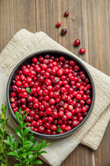 Fresh cranberries in a dark bowl on a wooden background with green branch and napkin.