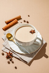 Traditional Indian masala chai tea with milk and spices in a cup on a beige background
