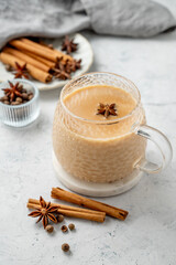 Traditional Indian masala chai tea with milk and spices in a cup on a light background with cinnamon