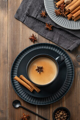 Traditional Indian masala chai tea with milk and spices in a black cup on a dark wooden background