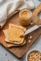 Peanut butter toast on a wooden board on a light background with scattered nuts, napkin and knife.