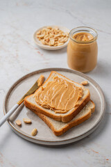 Peanut butter toast on a plate on a light marble background with nuts and knife.