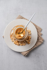 Creamy peanut butter in a jar on a light background with roasted nuts, spoon and napkin