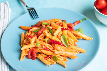 Classic penne all'Arrabbiata, spicy pasta with tomato and chilli sauce, on ceramic blue plate on blue kitchen table on sunny day