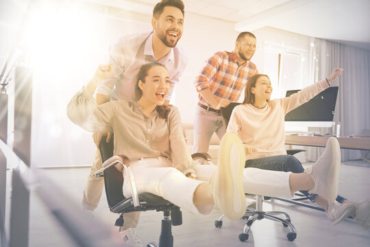 Group of happy coworkers riding chairs at workplace