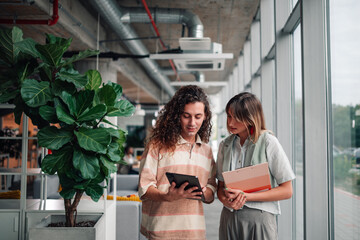 Colleagues collaborating using digital tablet in office hallway