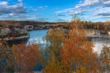 Golden and red trees surround still blue water under soft afternoon light. The mix of color,...