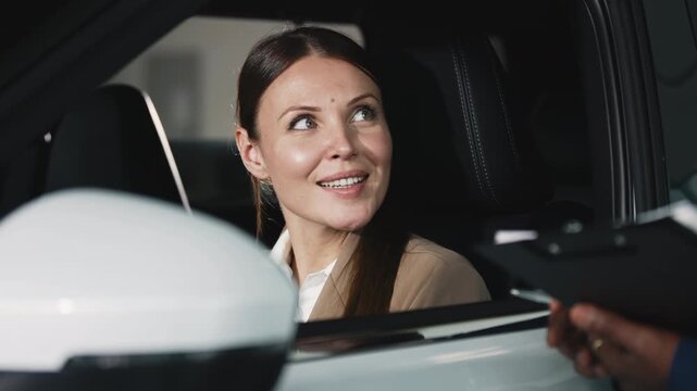 A young woman consults with a car dealer in a modern showroom about buying a new vehicle. Concept customer service and trust.