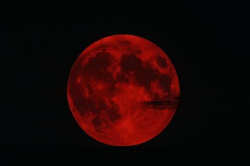 Fototapeta premium Dramatic blood red full moon rising above horizon with wisps of night clouds in dark sky