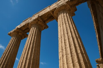 Fototapeta premium Ancient stone columns with weathered texture standing against blue sky architectural grandeur