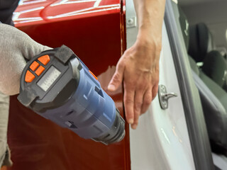 A specialist in wrapping a car with orange chameleon-colored vinyl film in the process of work. Car wrapping close-up. Car wrapping specialists cover the car with vinyl sheet or film. Selective focus.