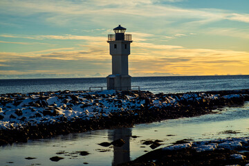 Lighthouse on snowy coast at sunset with calm sea