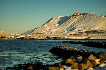 Golden winter sunlight over snow-covered mountain and calm coastal landscape