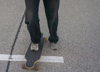 low angle close up of a persons feet in gray sneakers standing on a dark longboard on asphalt, white parking space line running under the board, concept of action sports