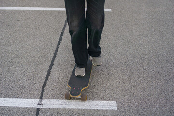 low angle close up of a persons feet in gray sneakers standing on a dark longboard on asphalt, white parking space line running under the board, concept of action sports