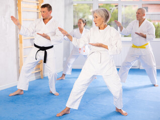 Active mature woman wearing kimono training karate techniques in group during workout session