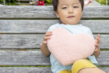ハートのクッションを持ってベンチに座る男の子（2歳、日本人）