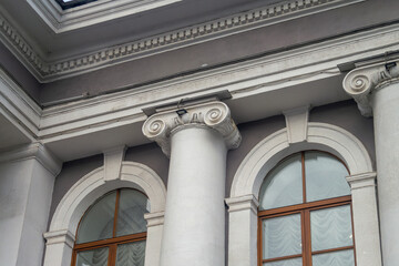 Facade fragment of an old classicism style building with Ionic columns and an arched window. Architectural background symbolizing justice, government, education, or culture and finance.