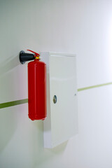 A red fire extinguisher is hanging on a white wall