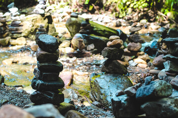 Stacked stones by a tranquil stream in a serene forest setting during daylight hours