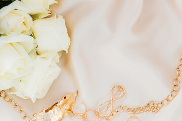 Elegant gold jewelry and white roses arranged on soft fabric for a romantic setting