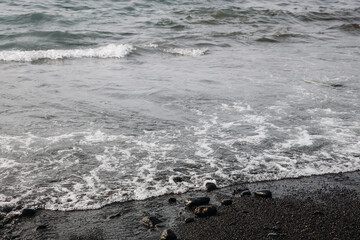 View of ocean wave with white bubbles on black volcanic beach.