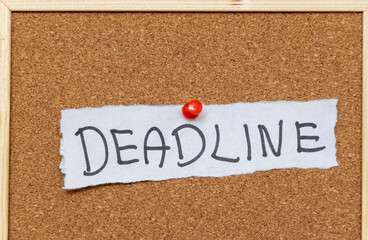 Handwritten text reading DEADLINE pinned on a corkboard. This image illustrates the concept of time constraints and urgency often faced in professional environments.