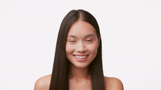 A beautiful young woman with long hair is pampering herself with hair care products, smiling gently against a plain background. The calm scene showcases her radiance and youthful glow.