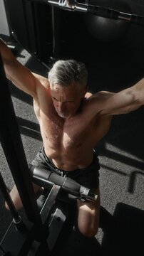 Vertical high angle view of strong senior Caucasian man doing lat pulldown exercise in modern gym