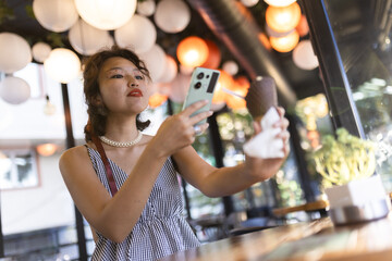 Young woman taking a photo with a smartphone while enjoying an ice cream cone in a modern café with hanging lights