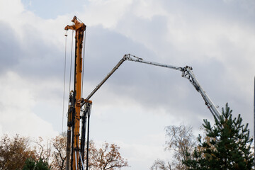Tall drilling rig and concrete pump working together on construction site with cloudy sky...