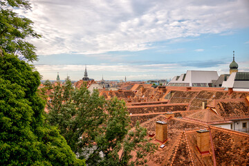 Obraz premium Graz, Austria – July 22, 2025: A view of the city’s rooftops and skyline from the Schlossberg hill, offering a picturesque overlook of the urban landscape below. 