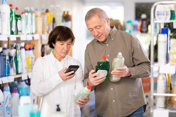 Elderly wife scans the barcode on the dishwashing detergent and shows it to her husband. Mature couple using qr code to pay for household items in supermarket