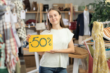 Teen girl in summer clothes posing with discount sign in clothing store