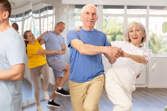 Group of elderly men and woman in sportswear learning to dance latin salsa dance in dance class - Powered by Adobe