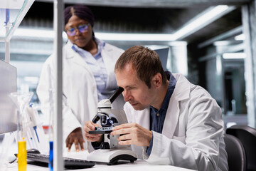 Diverse colleagues examine specimen under microscope lens with detailed focus in lab. Modern equipment and research study emphasize cellular observation and discovery in bioscience.