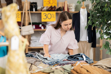Teenage girl buyer choosing jeans in clothing store
