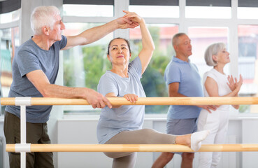 Professional senior male ballet trainer teaching group of dancers, helps to coordinate movements...